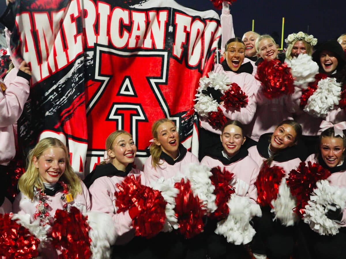 Cheer squad holding a printed D-Luxe blanket overhead at a night football game